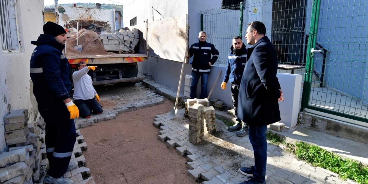 Bornova'da bir sokakta devam eden yol yenileme çalışması sırasında, biri koyu renk palto giymiş yetkili olmak üzere dört kişilik bir ekip, parke taşı döşenen alanı inceliyor. Arkada park halindeki bir kamyonun kasasında kum ve istiflenmiş parke taşları görülürken, işçilerden biri yerdeki taşları düzenliyor.