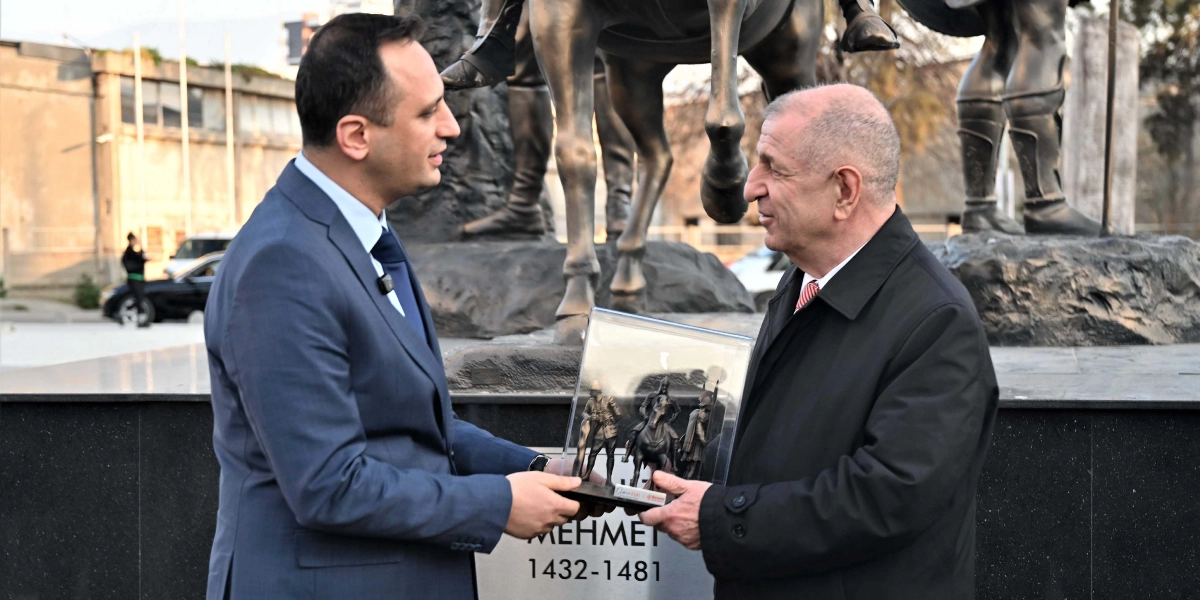 Ümit Özdağ, Abide-i Hürriyet Meydanı'ndaki Fatih Sultan Mehmet anıtının önünde, bir yetkiliden içerisinde atlı asker figürlerinin bulunduğu cam muhafazalı bir plaketi teslim alırken görülüyor.