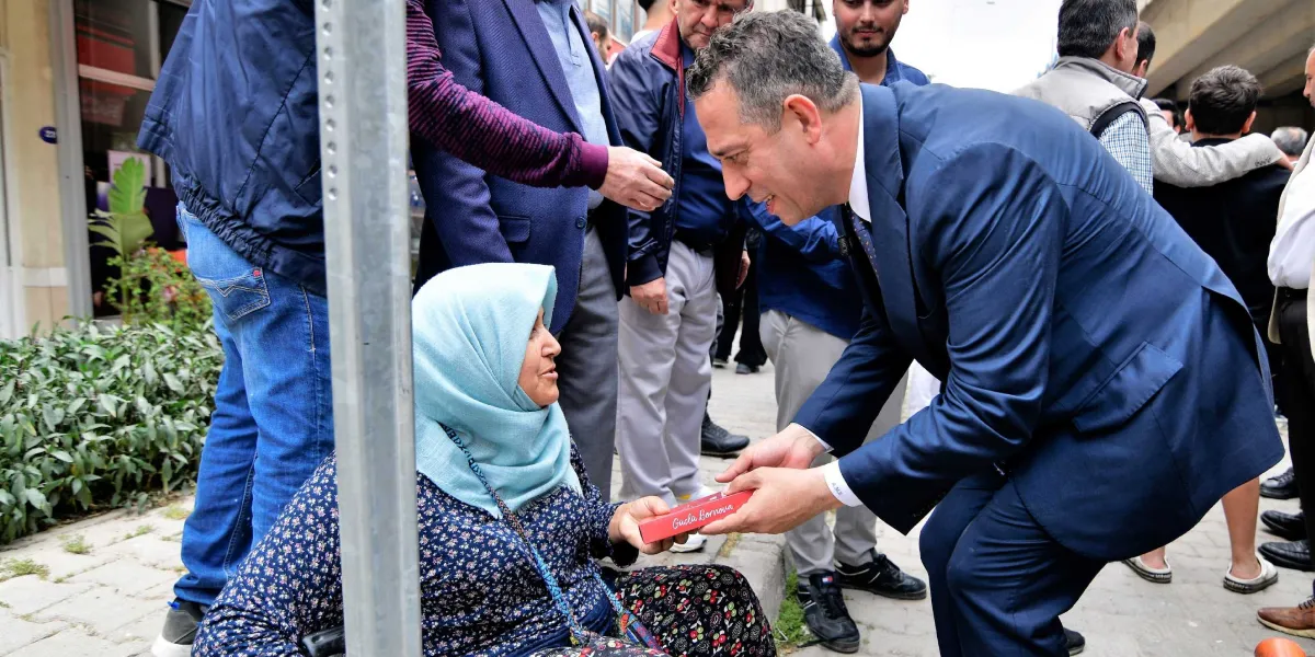 Lacivert takım elbiseli bir erkek, kaldırımda oturan başörtülü bir kadına üzerinde 