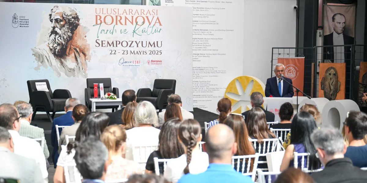 Uluslararası Bornova Tarih ve Kültür Sempozyumu'nun düzenlendiği salonda, konuşmacı kürsüsünde bir yetkili hitap ederken, sahnedeki protokol koltuklarından birinin üzerinde 