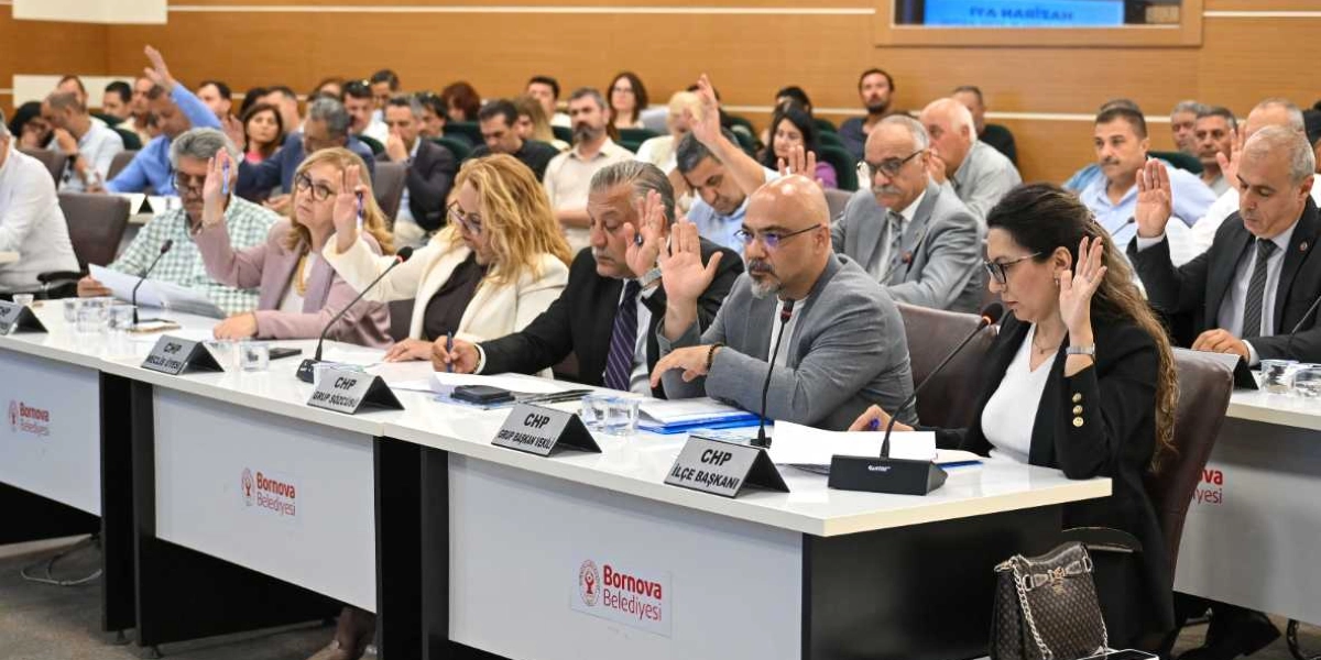 Bornova Belediyesi meclis toplantısında, masalarda oturan üyelerin oylama yapmak için ellerini kaldırdığı görülüyor. Ön sırada yer alan üyelerin önünde 