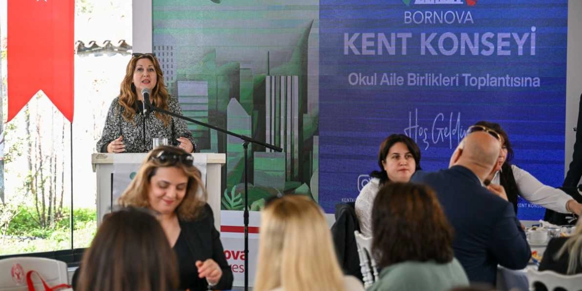 Bornova Kent Konseyi tarafından düzenlenen Okul Aile Birlikleri toplantısında, kürsüde konuşma yapan bir kadın ve onu dinleyen katılımcılar yer alıyor. Arka planda üzerinde 