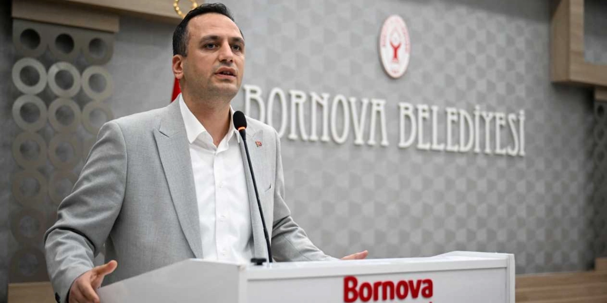Bornova Belediye Başkanı Ömer Eşki, üzerinde Bornova Belediyesi logosu ve yazısı bulunan bir kürsüde, arkasında Bornova Belediyesi yazılı gri bir duvar önünde konuşma yapıyor.
