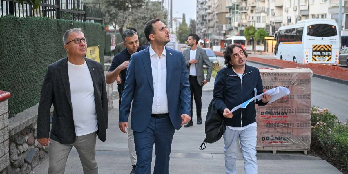 Bornova'da bir cadde üzerinde yürüyen dört erkek, çevrelerini inceleyerek bir saha incelemesi yapıyor. Önde mavi takım elbiseli bir kişi, yanında beyaz tişört ve gri ceket giymiş bir adam ile elinde belgeler tutan koyu renk ceketli başka bir kişi yer alıyor. Arkalarında ise gri ceketli bir kişi daha bulunuyor. Arka planda şehir trafiği ve üzerinde 