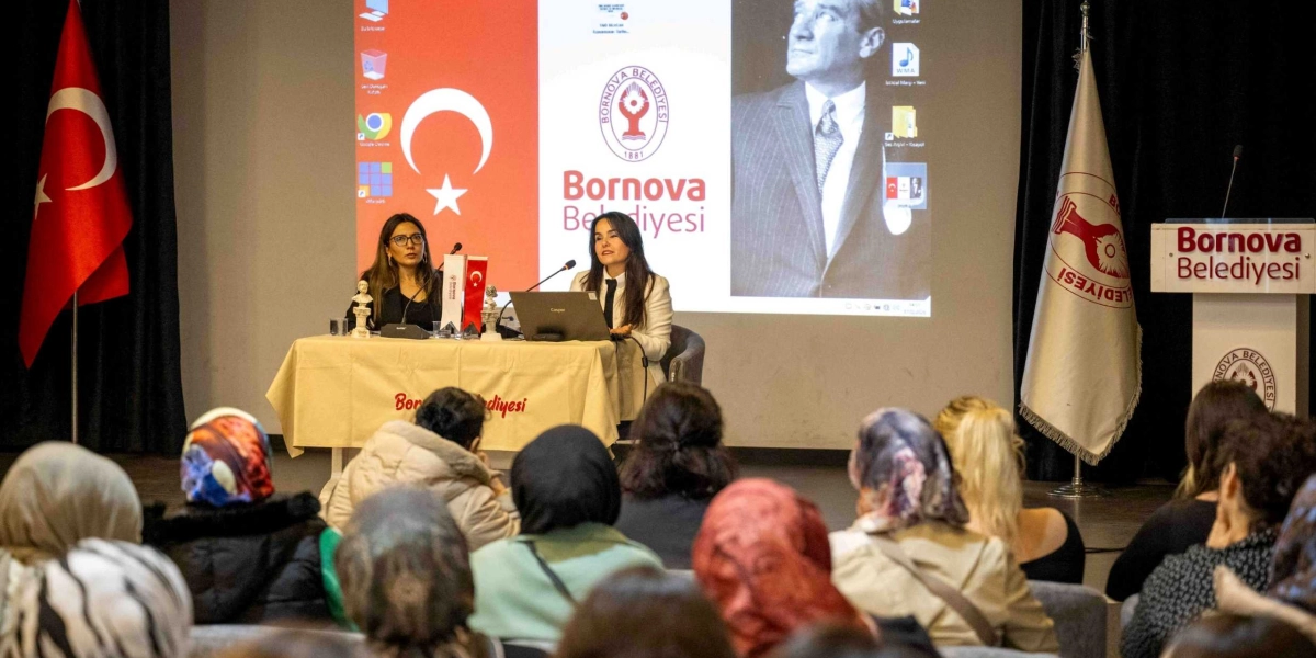 Bornova Belediyesi tarafından düzenlenen bir etkinlikte, sahnedeki masada oturan iki kadın konuşmacı, izleyici kitlesine hitap ediyor. Arka plandaki dev ekranda Türk bayrağı, Bornova Belediyesi logosu ve Mustafa Kemal Atatürk'ün bir fotoğrafı yer alıyor. Sahnenin solunda Türk bayrağı, sağında ise üzerinde Bornova Belediyesi yazan bir kürsü bulunuyor. İzleyiciler salonu doldurmuş durumda ve konuşmacıları dinliyor.