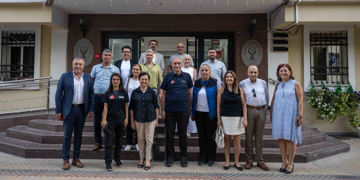 Bornova Belediyesi binasının önünde, afet bilinci konulu bir toplantı sonrası bir araya gelen, aralarında AFAD logolu kıyafetler giyen görevlilerin de bulunduğu yaklaşık 18 kişilik bir grup, merdivenlerin önünde yan yana durarak poz veriyor.