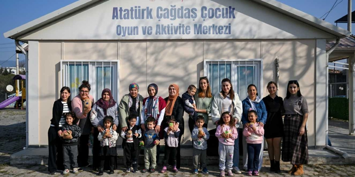 Atatürk Çağdaş Çocuk Oyun ve Aktivite Merkezi binasının önünde, ellerinde kendi yaptıkları çim adamlarla poz veren bir grup çocuk ve onlara eşlik eden yetişkinler.