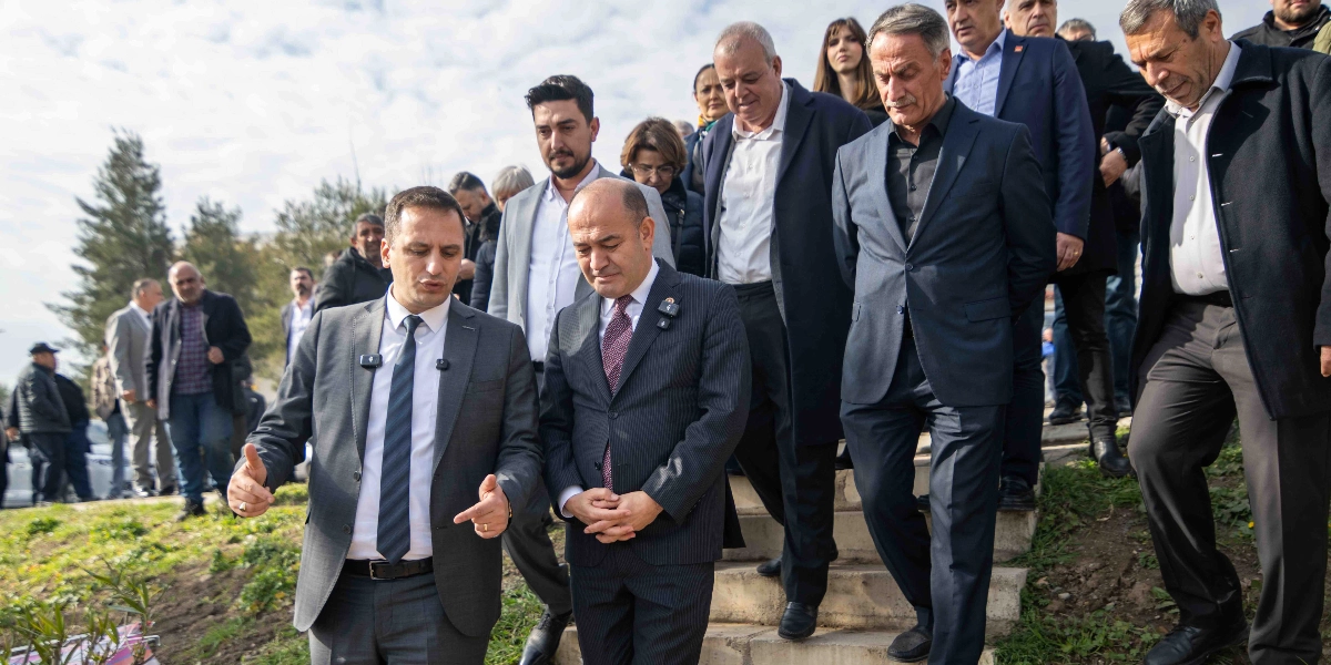 CHP Genel Başkan Yardımcısı Özgür Karabat ve Bornova Belediye Başkanı Ömer Eşki'nin de aralarında bulunduğu bir heyet, açık havada yürürken görülüyor. Önde, gri takım elbiseli ve kravatlı Özgür Karabat bir şeyler anlatırken, yanında koyu renk çizgili takım elbiseli ve kravatlı Ömer Eşki onu dinliyor. Arkalarında ise takım elbiseli diğer yetkililer ve katılımcılar, basamaklardan aşağı doğru inerek ilerliyor.
