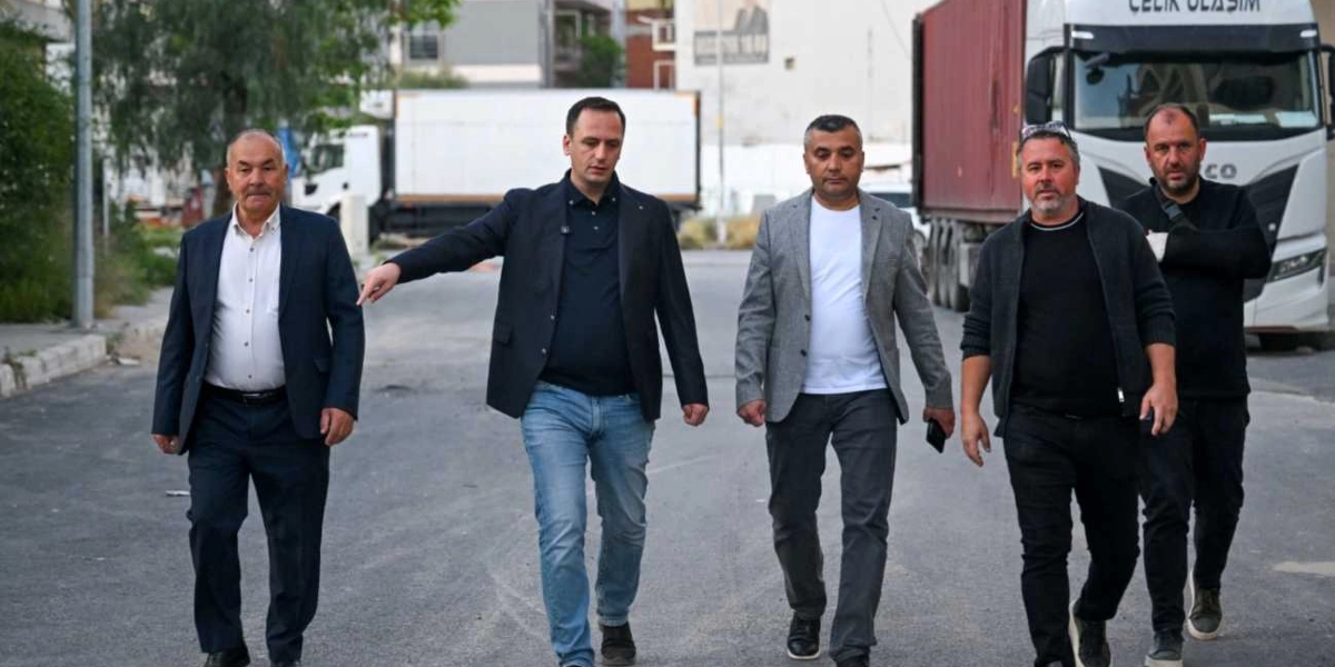 Beş kişilik bir grup, Egemenlik Mahallesi'ndeki bir sokakta yan yana yürürken görülüyor. Grubun önünde, lacivert ceketli ve kot pantolonlu bir erkek, eliyle ileriyi işaret ederek bir şeyler anlatıyor. Yanında koyu renk takım elbiseli bir bey, gri ceketli bir kişi ve siyah kıyafetli iki erkek daha bulunuyor. Arka planda park halindeki tırlar ve şehir dokusu yer alıyor.