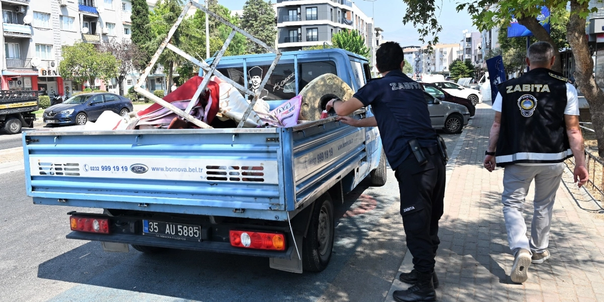 Bornova Belediyesi zabıta ekipleri, kaldırım üzerine bırakılan eşyaları toplayarak mavi renkli bir kamyonetin kasasına yüklüyor. Üzerinde 