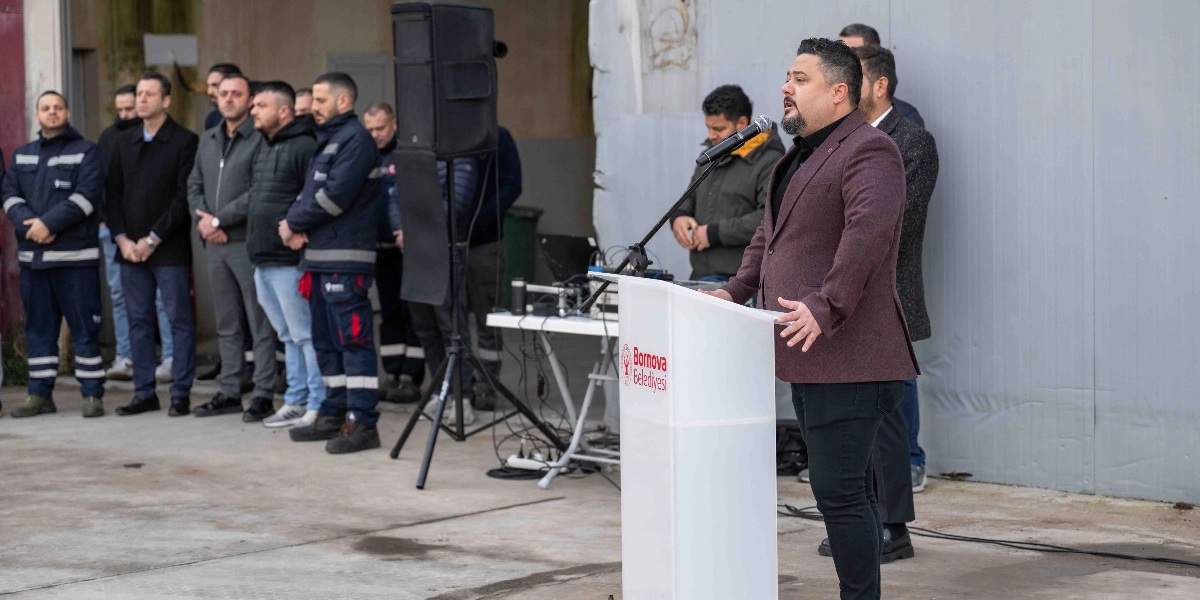 Bornova Belediye Başkanı Ömer Eşki, üzerinde Bornova Belediyesi logosu bulunan bir kürsüde mikrofon başında konuşma yaparken, karşısında sıralanmış belediye çalışanları onu dinliyor.