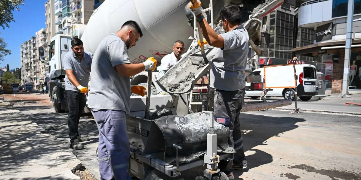 Bornova Belediyesi ekipleri, bir beton mikserinden aldıkları harcı, yol kenarına bordür döşemek için kullanılan özel bir makineye aktarıyor. İşçiler, koruyucu eldivenler takarak beton dökme ve yerleştirme işlemini gerçekleştiriyor.