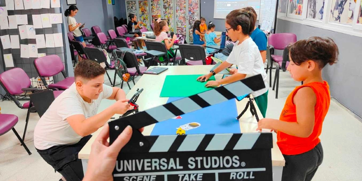 Bir atölye sınıfında stop-motion animasyon çalışması yapan çocuklar. Ön planda bir kişinin tuttuğu Universal Studios yazılı siyah bir film çekim klaketi yer alıyor. Masanın etrafındaki çocuklar, üzerinde figürler bulunan mavi ve yeşil zeminler üzerinde küçük oyuncaklarla çekim yapıyorlar. Arka planda ise mor sandalyeler, duvarda asılı çizimler ve diğer masalarda çalışan öğrenciler bulunuyor.