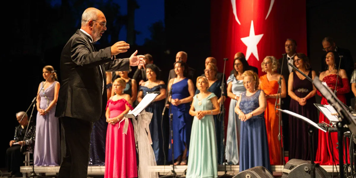 Siyah takım elbiseli bir orkestra şefi, sahne üzerinde arkasında büyük bir Türk bayrağı bulunan koroyu yönetiyor. Koro üyeleri, farklı renklerde şık gece elbiseleri giymiş kadınlardan ve takım elbiseli erkeklerden oluşuyor; hepsi önlerindeki nota sehpalarına bakarak şarkı söylüyor.