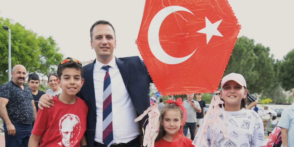 Lacivert takım elbiseli ve çizgili kravatlı bir erkek, yanında üzerinde Atatürk baskısı olan kırmızı tişörtlü bir erkek çocuk, kırmızı fiyonklu bir kız çocuğu ve desenli beyaz tişörtlü bir kız çocuğu ile birlikte gülümseyerek poz veriyor. Adamın elinde büyük, altıgen şeklinde kırmızı bir Türk bayrağı bulunuyor. Arka planda ise park ortamında bulunan diğer insanlar ve ağaçlar yer alıyor.