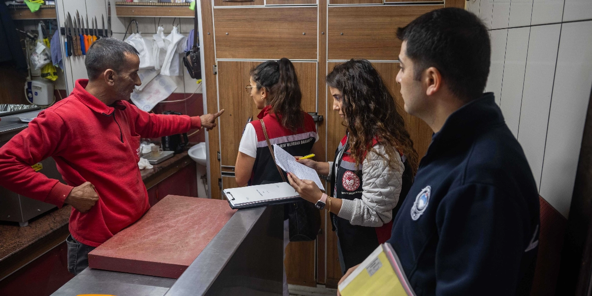 Tarım ve Orman Bakanlığı görevlileri, bir iş yerinde gıda denetimi yaparken kırmızı kıyafetli bir çalışanla görüşüyor. Görevliler ellerindeki evrakları incelerken, iş yeri çalışanı bir noktayı işaret ederek açıklama yapıyor.