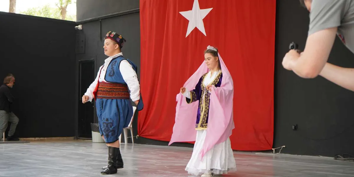 Geleneksel Türk kıyafetleri giymiş down sendromlu bir genç erkek ve genç kadın, arkalarında asılı büyük kırmızı Türk bayrağı önünde dans ediyor. Erkek dansçı mavi yelek, şalvar, işlemeli kuşak ve siyah çizmeler giymiş; kadın dansçı ise mor işlemeli bir kaftan, beyaz etek ve başının üzerinde pembe bir duvakla görünüyor. Sağ tarafta bir kişinin elleri ve kamerası kadraja girerken, sol tarafta ise bir izleyici ayakta duruyor.