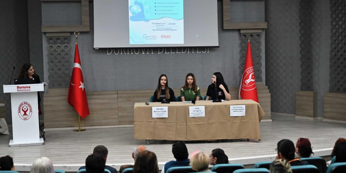 Bornova Belediyesi Nevzat Kavaklı Kültür Merkezi'nde düzenlenen bir panelde, kürsüde konuşan bir kadın ve masada oturan üç genç kız öğrenci yer alıyor. Masanın önünde Melike Beyza Eşlik, Ayşe Tutkun ve Nil Sultan Can isimlerinin ve okullarının yazılı olduğu etiketler bulunuyor. Arka planda dev bir ekranda 