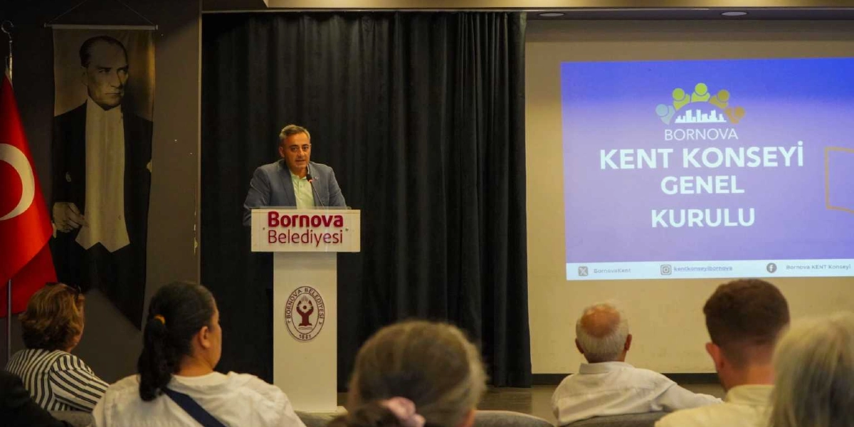Bornova Belediyesi kürsüsünde konuşma yapan bir yetkili, arkasında Mustafa Kemal Atatürk portresi ve Türk bayrağı ile sağ tarafta üzerinde 