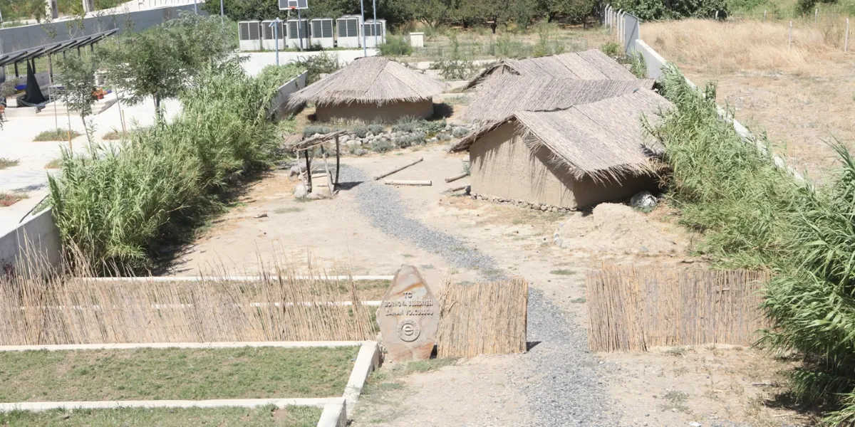 Yeşilova Höyüğü'nde sazdan çatılı geleneksel evlerin bulunduğu açık hava müzesi alanı. Ön planda, üzerinde 