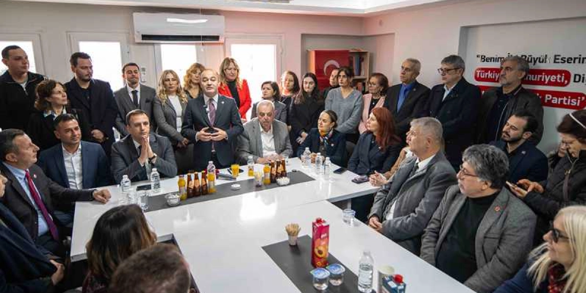 CHP Genel Başkan Yardımcısı Özgür Karabat'ın bir toplantı masasında ayakta konuşma yaptığı, çevresinde ise çok sayıda kişinin dinleyici olarak yer aldığı toplantı ortamı. Masanın üzerinde içecekler ve atıştırmalıklar bulunurken, arka planda duvarda 