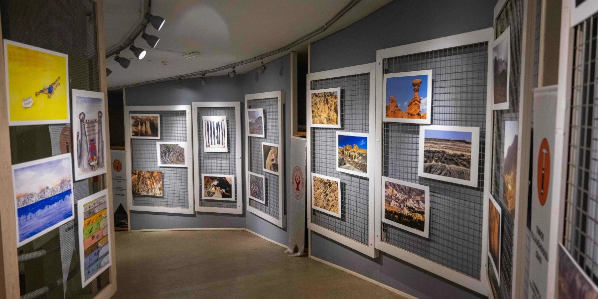 Bornova'da bir sergi salonunda, duvarlara monte edilmiş metal ızgara paneller üzerinde çeşitli jeolojik oluşumları, kaya yapılarını ve doğa manzaralarını gösteren fotoğraflar ile bazı çizimlerin sergilendiği bir alan. Sergi alanının duvarları gri renkte olup, tavandaki spot ışıklarıyla aydınlatılmıştır. Panellerin üzerinde Bornova Belediyesi'nin logosu ve 