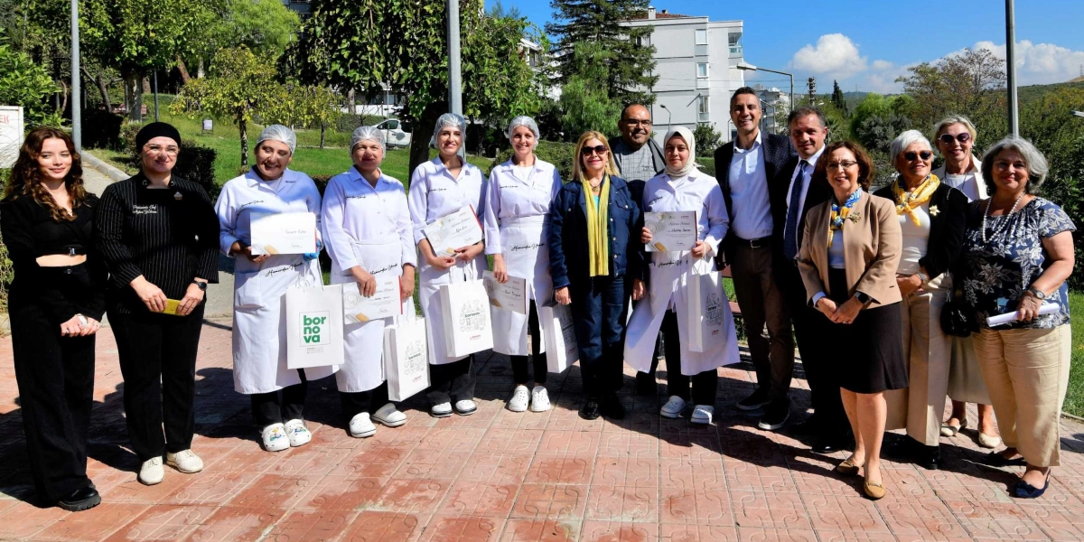 Açık havada, park benzeri bir alanda yan yana duran, aralarında beyaz önlük ve bone giymiş kursiyerlerin, eğitmenlerin ve yetkililerin bulunduğu kalabalık bir grup. Kursiyerler ellerinde sertifikalarını ve üzerinde 