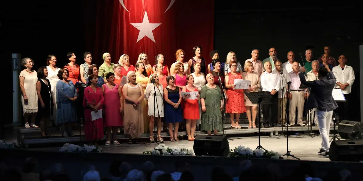 Sahne üzerinde, arkalarında büyük bir Türk bayrağı asılı olan kalabalık bir koro, ellerinde notalarla şarkı söylüyor. Kadın ve erkeklerden oluşan koro üyeleri şık kıyafetler giymiş durumda. Sahnenin sağ tarafında, sırtı izleyicilere dönük olan şef, koroyu yönetiyor. Sahne önünde ses sistemleri ve mikrofonlar bulunuyor.
