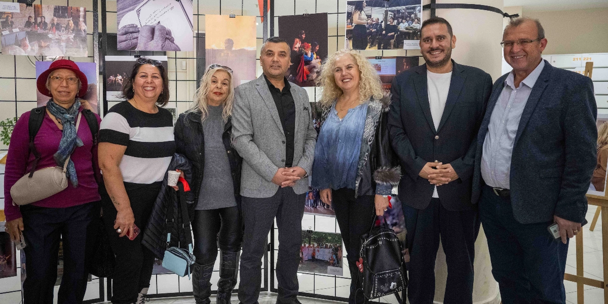 Bornova’da düzenlenen Birlikte Mümkün sergisinde, arka planda çeşitli fotoğrafların asılı olduğu bir panonun önünde yan yana duran yedi kişilik bir grup. Grupta yer alan dört kadın ve üç erkek, gülümseyerek kameraya bakıyor. Kadınlardan biri kırmızı şapkalı, diğeri ise sarı kıvırcık saçlı. Erkeklerden ikisi ceket giymiş, biri ise daha resmi bir takım elbise içerisinde. Ortam, bir sergi salonu veya etkinlik alanı atmosferini yansıtıyor.