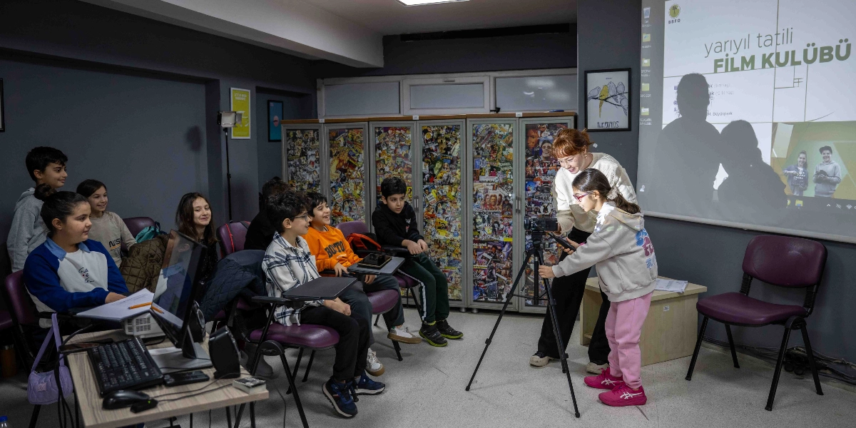 Bir grup çocuğun katıldığı film atölyesinde, bir eğitmen eşliğinde tripod üzerindeki profesyonel kamerayı kullanan kız çocuğu, çekim yapmayı öğreniyor. Sınıf ortamındaki diğer çocuklar ilgiyle izlerken, arka plandaki projeksiyon perdesinde 