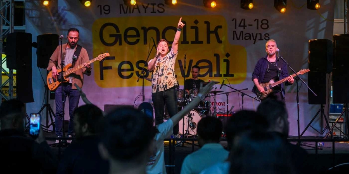 19 Mayıs Gençlik Festivali kapsamında sahnede performans sergileyen bir müzik grubu. Grubun solisti elini havaya kaldırarak şarkı söylerken, yanında bas gitarist, elektro gitarist ve davulcu eşlik ediyor. Arka planda 
