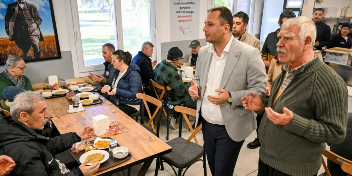 Bornova Belediyesi'ne ait bir yemekhanede, masalarda oturan vatandaşlar ve ayakta duran bir yetkili dua ediyor. Masalarda yemek tepsileri, nohut ve pilav gibi yiyecekler bulunuyor. Duvarlarda Atatürk portresi ve 