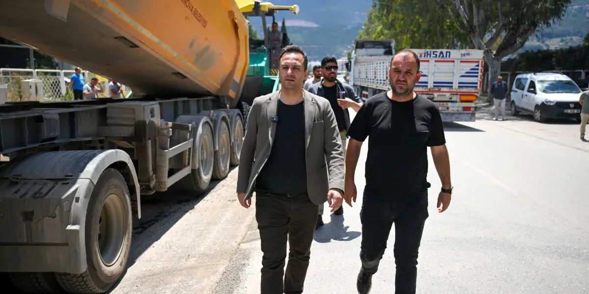 Pınar Caddesi'ndeki yol yenileme çalışmaları sırasında, yanlarında büyük bir hafriyat kamyonu bulunan iki erkek yetkili caddede yürüyerek incelemelerde bulunuyor.
