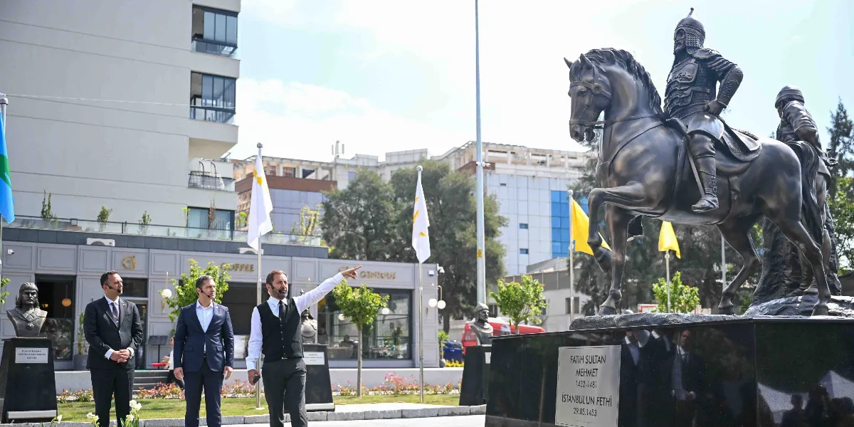 Bornova'da bir meydanda, üzerinde Fatih Sultan Mehmet'in atlı heykelinin bulunduğu kaidenin önünde duran üç erkekten biri eliyle ileriyi işaret ederken, diğer ikisi onu dinliyor. Heykelin kaidesinde 
