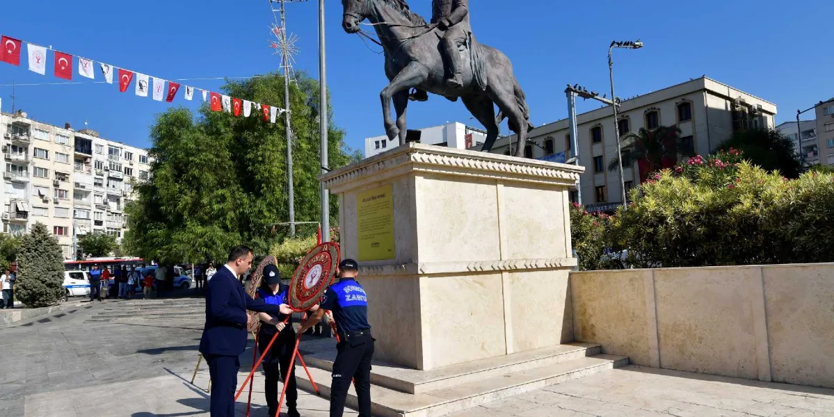 Açık havada, üzerinde Atatürk'ün atlı heykelinin bulunduğu yüksek bir kaidenin önünde, resmi kıyafetli iki zabıta memuru ve takım elbiseli bir kişi, üzerinde Türk bayrağı amblemi bulunan çelengi kaidenin önüne yerleştiriyor. Meydanın çevresi Türk bayraklarıyla süslenmiş, arka planda ise şehir binaları ve ağaçlar yer alıyor.