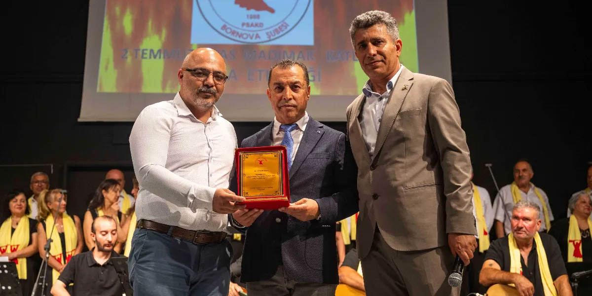 Kapalı bir sahnede, arkada üzerinde PSAKD Bornova Şubesi logosu ve 