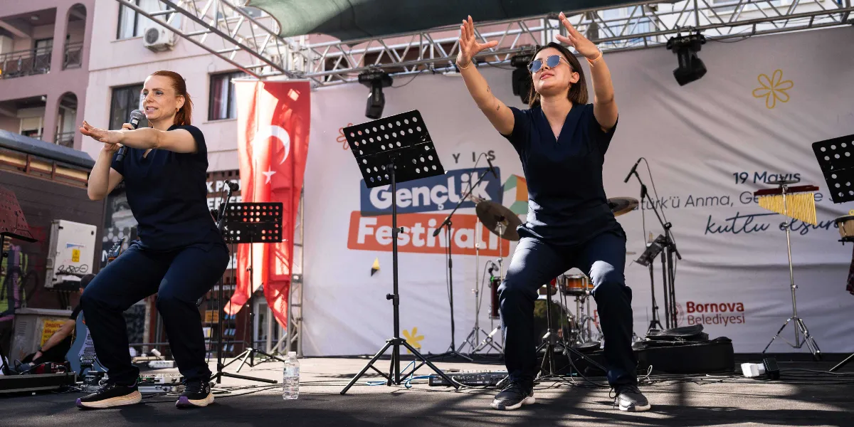 Açık havada kurulan bir sahnede, lacivert üniformalar giymiş iki kadın, müzik eşliğinde squat hareketi yaparak dans ediyor. Sağdaki kadın güneş gözlüğü takıyor ve ellerini havaya kaldırarak ritme eşlik ediyor, soldaki kadın ise elinde bir mikrofon tutuyor. Arka planda üzerinde 