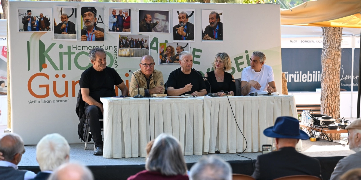 Bornova Kitap Günleri kapsamında Attila İlhan anısına düzenlenen bir panelde, beyaz örtülü bir masada yan yana oturan beş konuşmacı izleyicilere hitap ediyor. Arka planda üzerinde 
