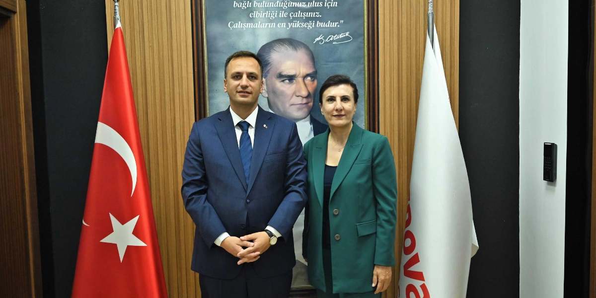 Lacivert takım elbiseli bir erkek ile yeşil ceketli bir kadının, arkalarında Mustafa Kemal Atatürk'ün portresi ve üzerinde 