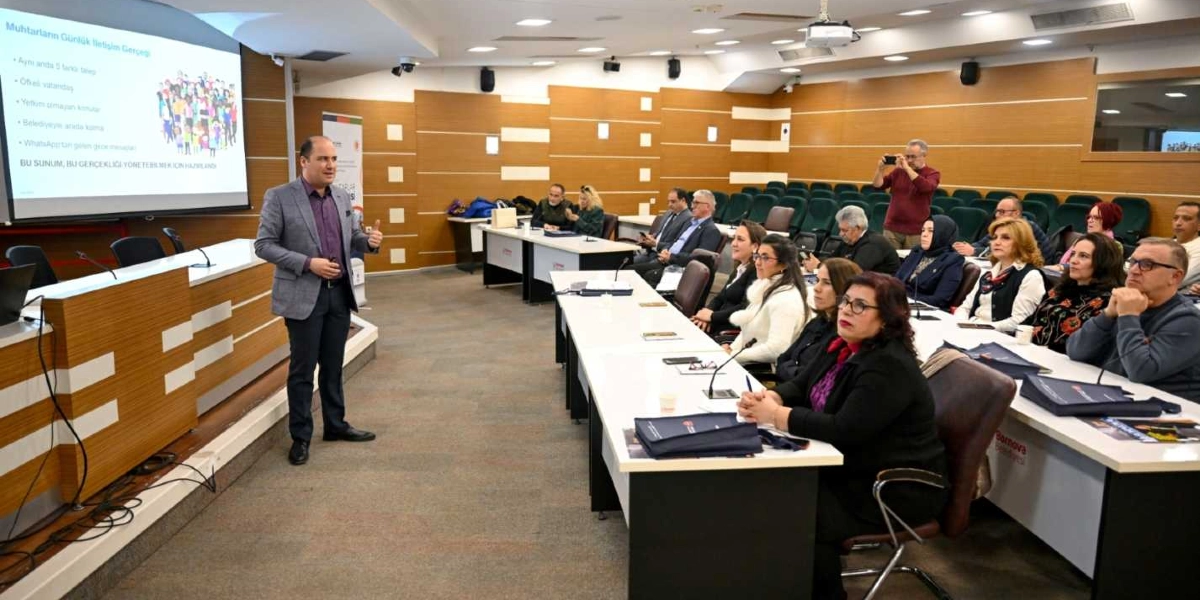 Modern bir konferans salonunda, gri ceketli bir konuşmacı, 