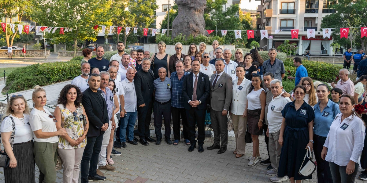 Açık havada, park benzeri bir alanda bir araya gelmiş, çoğunluğu resmi kıyafetli veya yakalarında Srebrenitsa soykırımını simgeleyen 