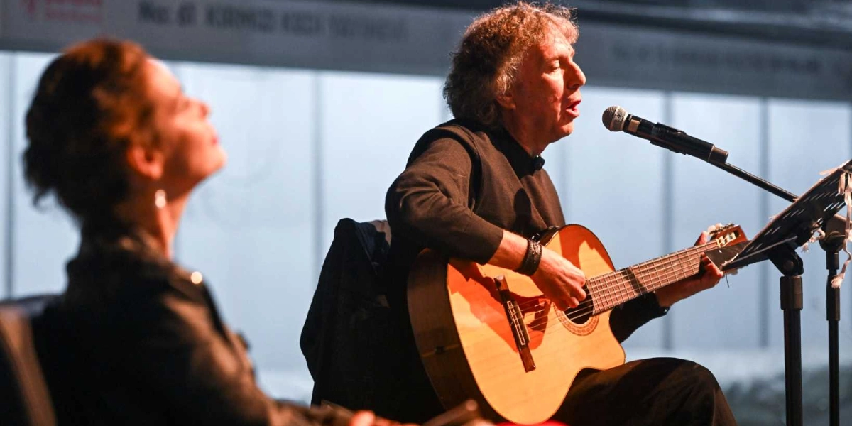Sahnede akustik gitar çalan ve mikrofon başında şarkı söyleyen kıvırcık saçlı bir erkek ile ona eşlik eden, profilden görünen bir kadın sanatçı yer alıyor.