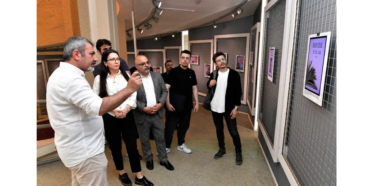 Bornova'daki bir sergi alanında, beyaz gömlekli bir erkek, duvarda asılı olan Orhan Kemal'in 