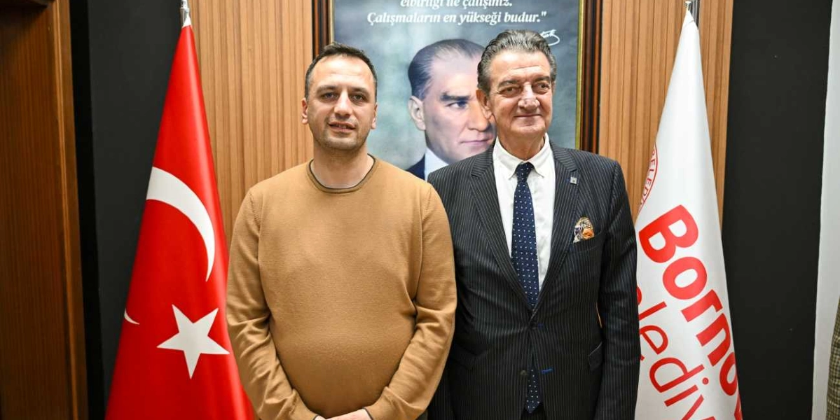 Bej renkli kazak giyen bir erkek ile lacivert çizgili takım elbiseli ve kravatlı bir erkek, arkalarında Mustafa Kemal Atatürk'ün portresi, yanlarında ise Türk bayrağı ve Bornova Belediyesi bayrağı ile yan yana duruyor.