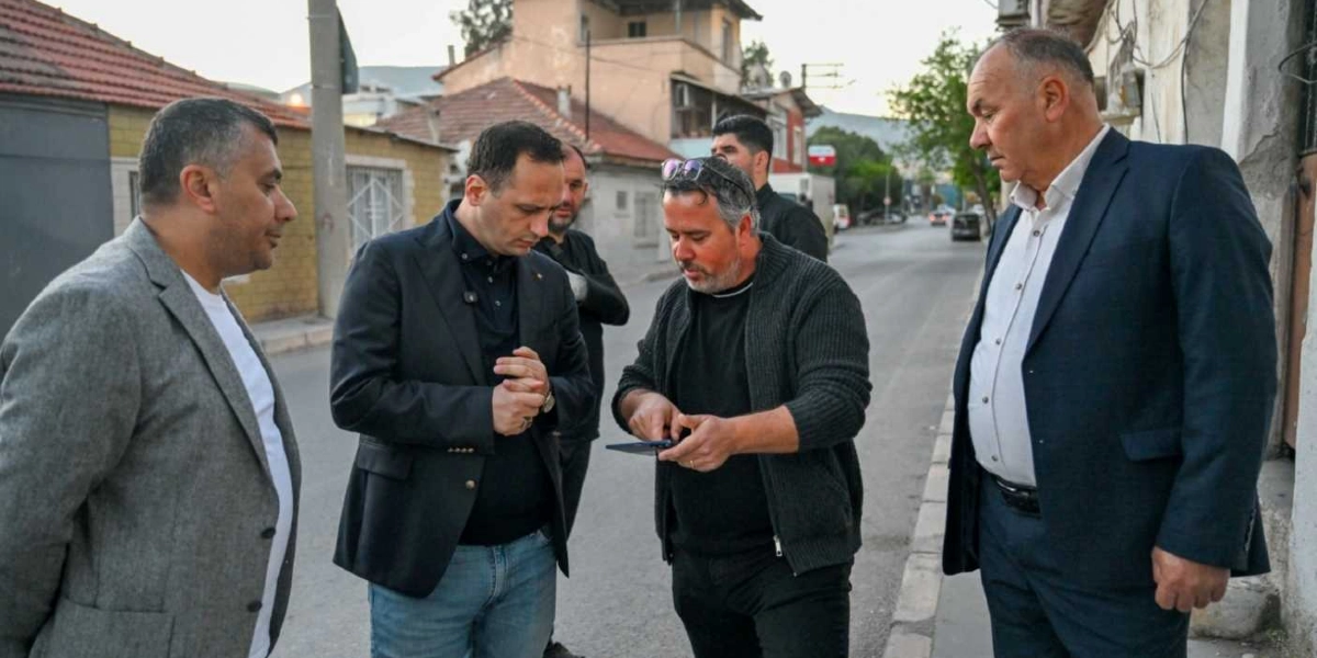 Egemenlik Mahallesi'ndeki bir sokakta, aralarında Başkan Eşki'nin de bulunduğu beş kişilik bir grup, ellerindeki bir mobil cihazı inceleyerek saha çalışması yapıyor. Başkan Eşki ve yanındaki diğer kişiler, gündelik kıyafetler ve ceketlerle sokakta durmuş, dikkatle ekrana bakarak bir konu üzerinde değerlendirmede bulunuyor.