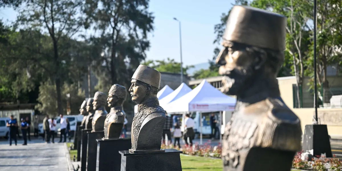 Bornova'da bir parkta yan yana dizilmiş, Osmanlı ve Cumhuriyet dönemi devlet adamlarını temsil eden bronz büstler. Ön planda odaklanmış bir büst yer alırken, arkaya doğru sıralanan diğer büstler derinlik algısıyla bulanıklaşmaktadır. Arka planda beyaz çadırlar, ağaçlar ve yürüyen insanlar görülmektedir.