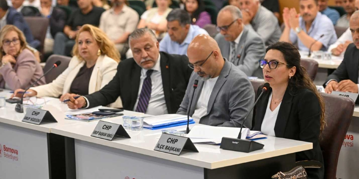 Bornova Belediyesi meclis toplantısında, masada yan yana oturan ve önlerinde isimlikleri bulunan CHP temsilcileri yer alıyor. En öndeki masada soldan sağa doğru; CHP Grup Sözcüsü, CHP Grup Başkan Vekili, CHP İlçe Başkanı ve yanında bir kadın katılımcı oturuyor. Katılımcıların önünde mikrofonlar, dosyalar ve Bornova Belediyesi logosu bulunan bir masa düzeni görülüyor. Arka planda ise toplantıyı takip eden diğer katılımcılar bulunuyor.