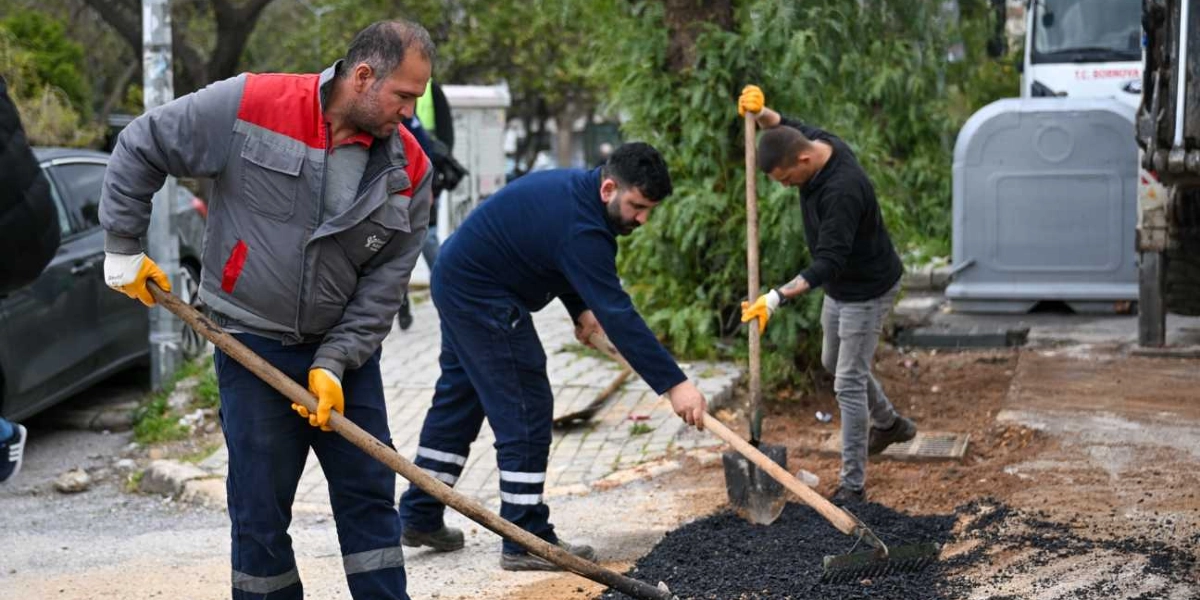 Bornova Belediyesi personeli, ellerinde kürek ve tırmıklarla kaldırım kenarındaki toprak zemine asfalt sererek çevre düzenleme çalışması yapıyor.