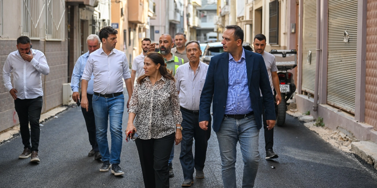 Bornova'da yeni asfaltlanmış bir sokakta yürüyen, aralarında Bornova Belediye Başkanı Ömer Eşki'nin de bulunduğu bir grup yetkili ve vatandaş. Grup, incelemelerde bulunmak üzere sokağın ortasında ilerliyor.
