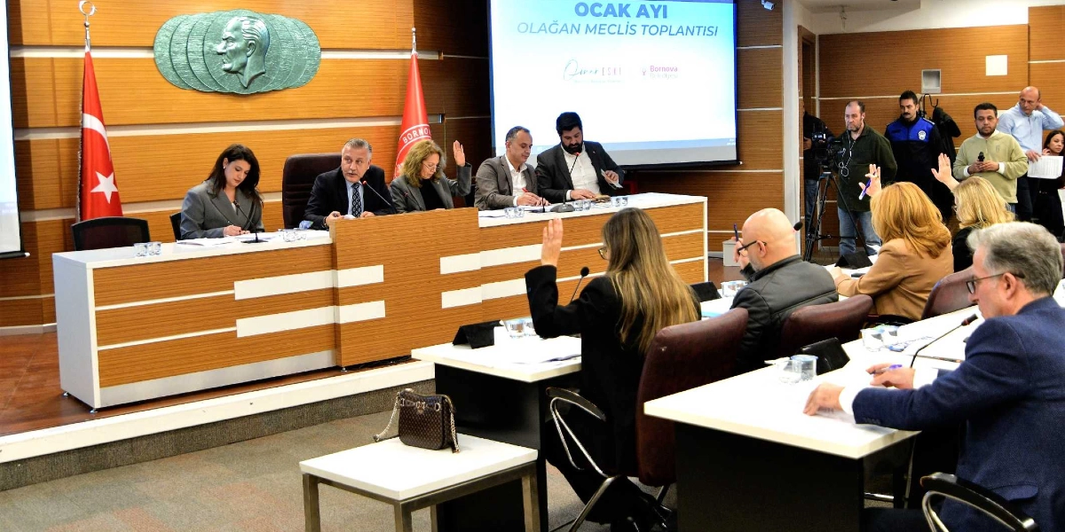 Bornova Belediyesi meclis salonunda gerçekleşen Ocak ayı olağan meclis toplantısında, katılımcılar masalarda otururken bazı üyeler oylama için ellerini kaldırıyor. Arka planda duvarda Atatürk kabartması, yanında Türk bayrağı ve Bornova Belediyesi flaması yer alıyor. Salonun ön kısmındaki dev ekranda 